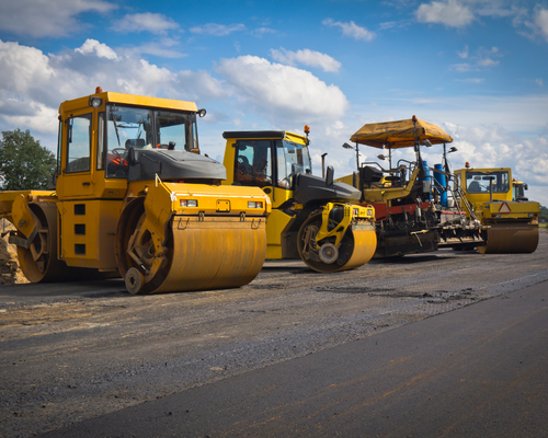 yellow asphalt rollers lined next to each other in front of paved road